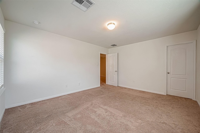 unfurnished room with baseboards, visible vents, and light colored carpet