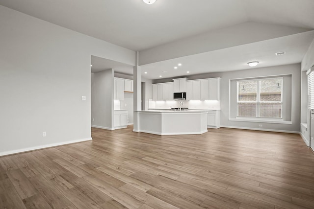 unfurnished living room with vaulted ceiling, sink, and light hardwood / wood-style floors