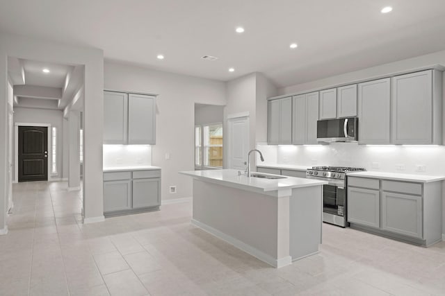 kitchen with gray cabinetry, sink, an island with sink, and appliances with stainless steel finishes