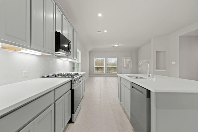 kitchen with sink, decorative backsplash, light tile patterned floors, stainless steel appliances, and a center island with sink