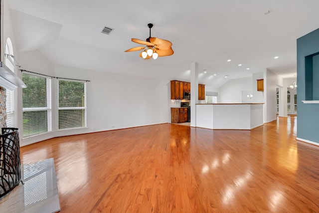 unfurnished living room with ceiling fan with notable chandelier, vaulted ceiling, and light hardwood / wood-style floors