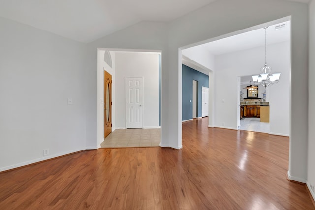 empty room featuring lofted ceiling, light wood-type flooring, and a notable chandelier