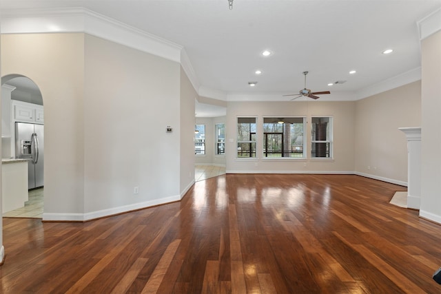 unfurnished living room featuring arched walkways, ceiling fan, dark wood-style flooring, baseboards, and crown molding