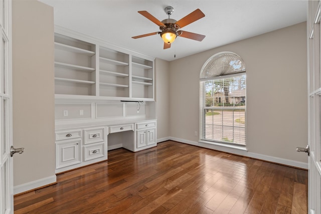 unfurnished office with dark wood-style floors, built in desk, and baseboards