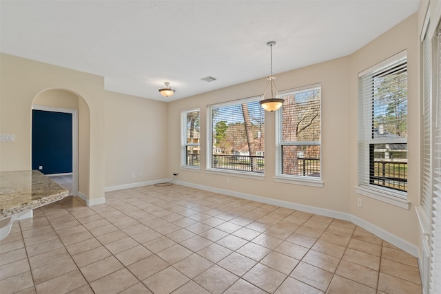 unfurnished dining area with arched walkways, baseboards, and light tile patterned floors