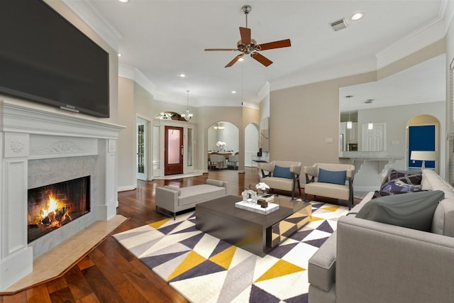 living room with arched walkways, light wood finished floors, visible vents, ornamental molding, and a tile fireplace