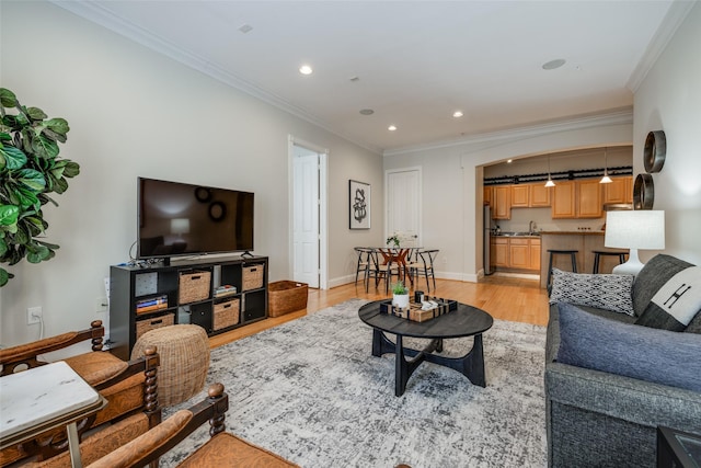 living room with ornamental molding, sink, and light wood-type flooring