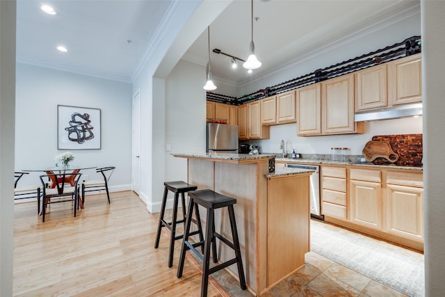 kitchen with appliances with stainless steel finishes, light stone countertops, a kitchen island, light brown cabinetry, and decorative light fixtures