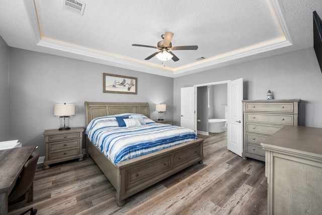 bedroom with ensuite bathroom, dark hardwood / wood-style floors, a textured ceiling, and a tray ceiling