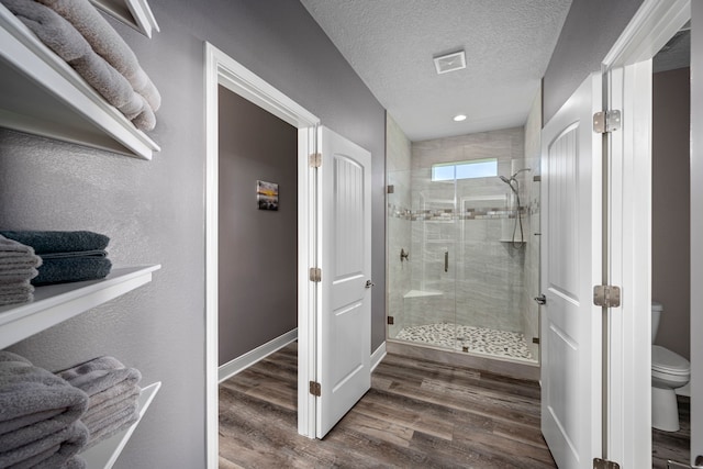 bathroom with walk in shower, wood-type flooring, toilet, and a textured ceiling