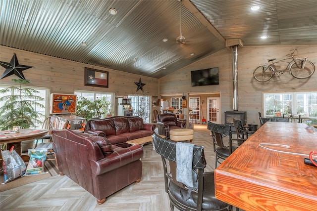 living room with wood walls, high vaulted ceiling, a wood stove, ceiling fan, and light parquet floors