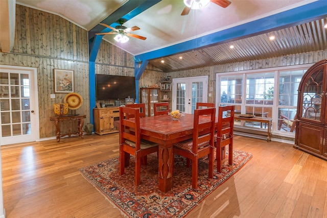 dining space with beam ceiling, wooden walls, light hardwood / wood-style floors, and french doors