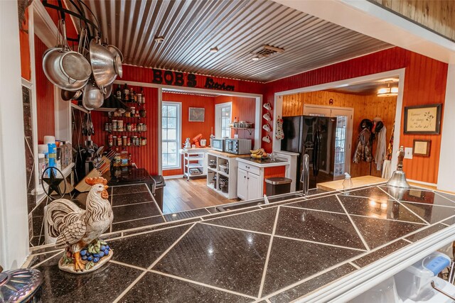 kitchen featuring white cabinetry, dark wood-type flooring, wooden walls, and black refrigerator with ice dispenser