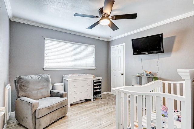 bedroom featuring crown molding, light hardwood / wood-style flooring, a nursery area, and ceiling fan