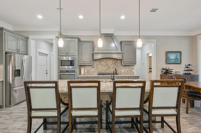 kitchen with appliances with stainless steel finishes, decorative light fixtures, a kitchen island with sink, and custom exhaust hood