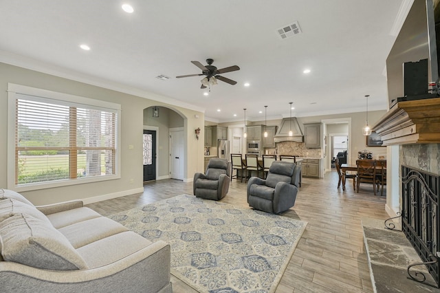 living room with crown molding, ceiling fan, a tiled fireplace, and light hardwood / wood-style flooring