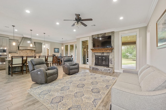 living room featuring crown molding, ceiling fan, a fireplace, and light hardwood / wood-style flooring