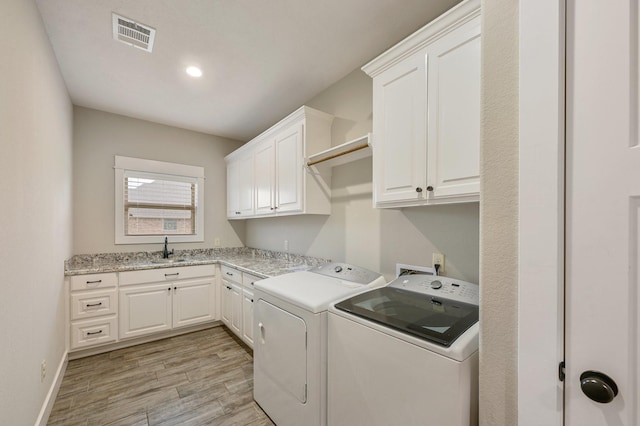 clothes washing area with separate washer and dryer, sink, cabinets, and light wood-type flooring