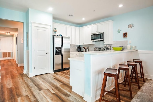 kitchen with stainless steel appliances, white cabinets, decorative backsplash, kitchen peninsula, and light wood-type flooring