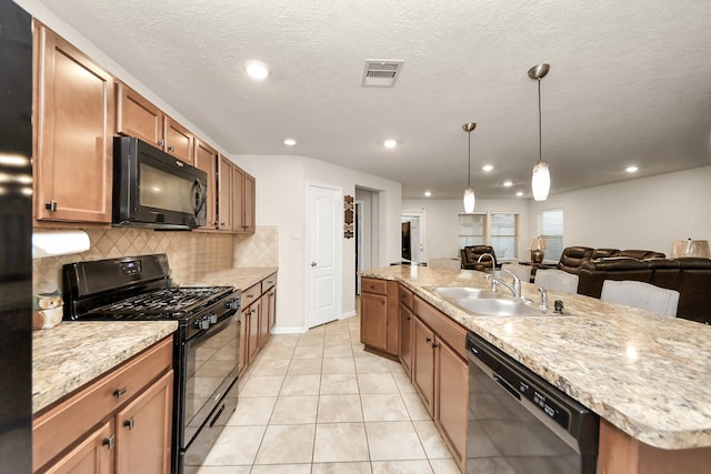 kitchen with sink, backsplash, light tile patterned floors, black appliances, and a center island with sink