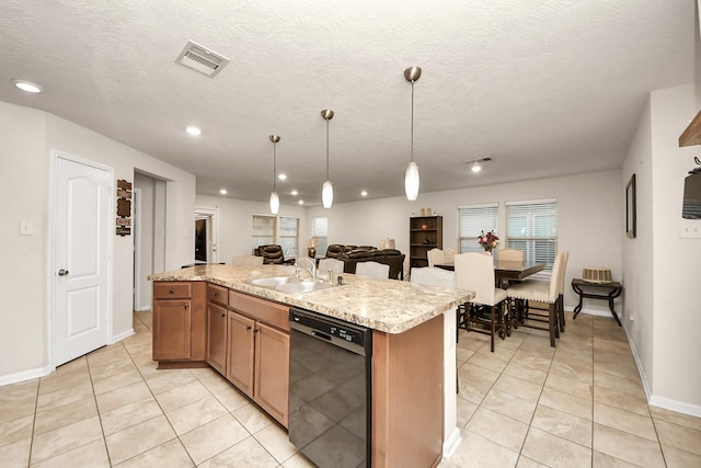 kitchen with light tile patterned flooring, light stone counters, hanging light fixtures, dishwasher, and a kitchen island with sink