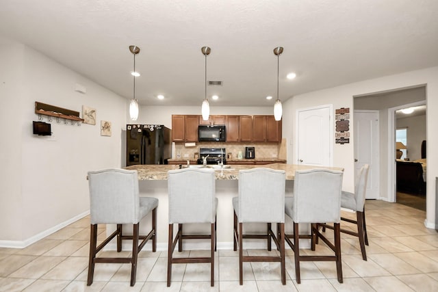 kitchen with decorative light fixtures, a kitchen breakfast bar, a kitchen island with sink, decorative backsplash, and black appliances