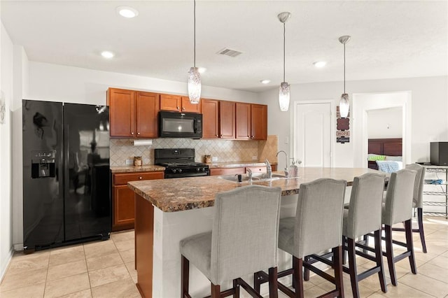 kitchen with a kitchen island with sink, pendant lighting, a kitchen breakfast bar, and black appliances