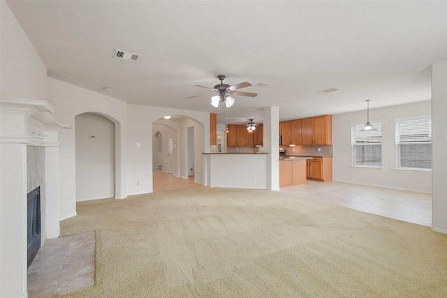 unfurnished living room featuring ceiling fan, light colored carpet, and a fireplace