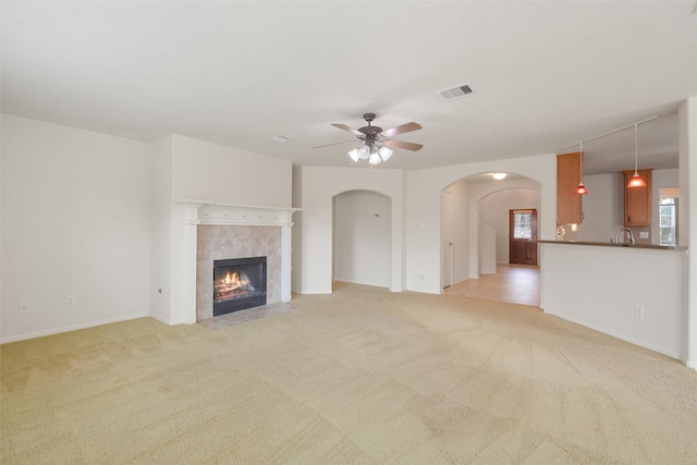 unfurnished living room with ceiling fan, a tile fireplace, and light carpet