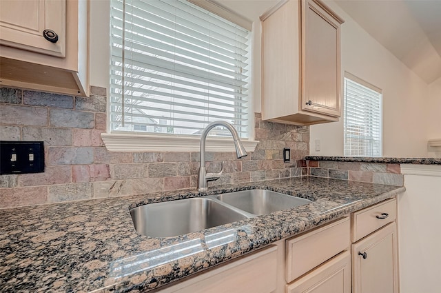 kitchen with cream cabinets, dark stone counters, sink, and decorative backsplash