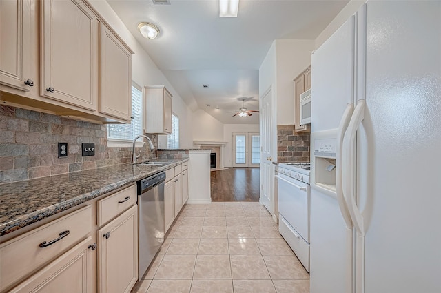 kitchen with light tile patterned flooring, sink, dark stone countertops, white appliances, and decorative backsplash