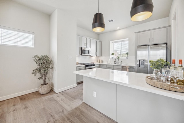 kitchen featuring gray cabinetry, light wood-type flooring, kitchen peninsula, pendant lighting, and stainless steel appliances