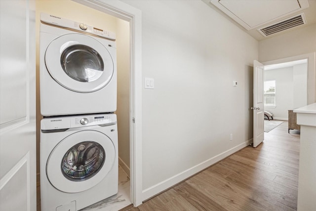 laundry room with stacked washing maching and dryer and light hardwood / wood-style flooring