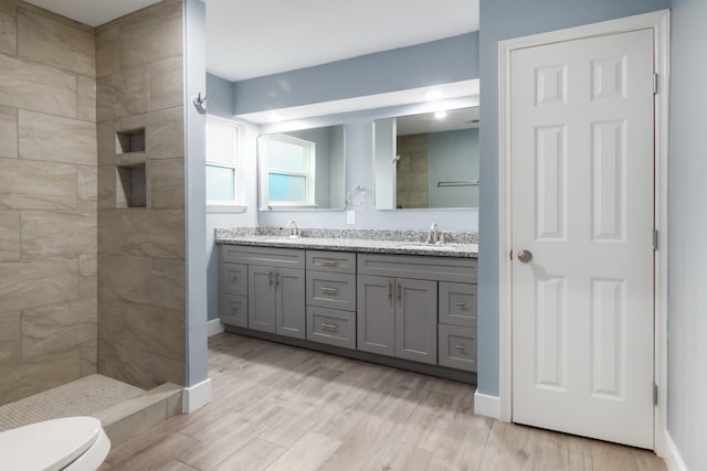 bathroom with toilet, tiled shower, wood-type flooring, and vanity