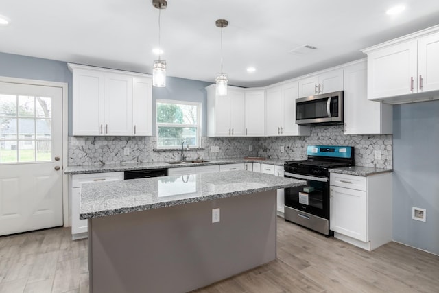 kitchen with white cabinetry, stainless steel appliances, hanging light fixtures, light stone countertops, and sink