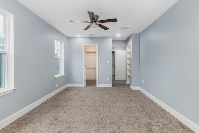 unfurnished bedroom featuring ceiling fan, a walk in closet, and carpet floors