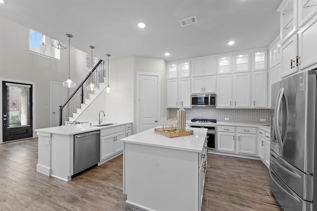 kitchen featuring a kitchen island, white cabinetry, sink, hanging light fixtures, and stainless steel appliances