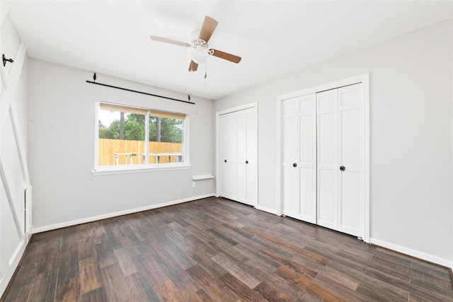 unfurnished bedroom featuring multiple closets, ceiling fan, and dark hardwood / wood-style floors