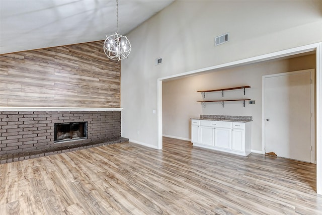 unfurnished living room with high vaulted ceiling, a brick fireplace, a chandelier, and light hardwood / wood-style floors