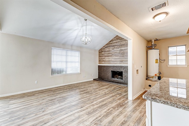 unfurnished living room with light hardwood / wood-style flooring, water heater, a brick fireplace, vaulted ceiling, and a chandelier