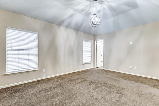 empty room with an inviting chandelier, a textured ceiling, a healthy amount of sunlight, and carpet flooring