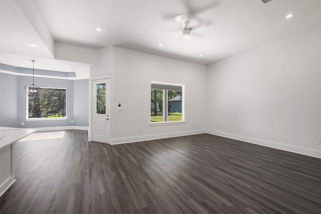 unfurnished living room featuring a raised ceiling, ceiling fan with notable chandelier, and dark hardwood / wood-style flooring