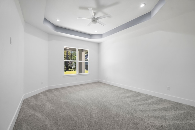 empty room with a tray ceiling, ceiling fan, and carpet flooring