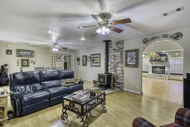 living room featuring ceiling fan, a fireplace, a textured ceiling, and light hardwood / wood-style flooring