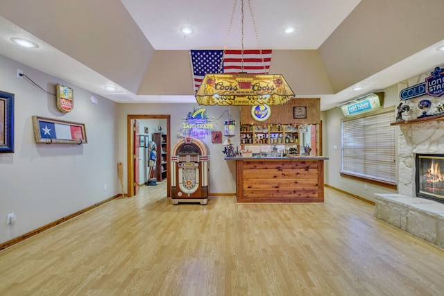 kitchen with a raised ceiling, a stone fireplace, and hardwood / wood-style floors