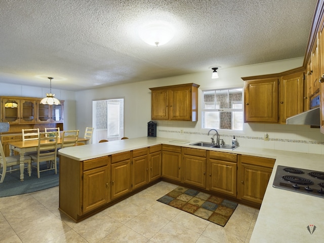 kitchen with brown cabinets, decorative light fixtures, a peninsula, light countertops, and a sink