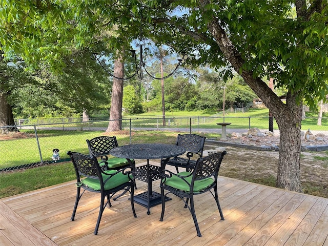 wooden terrace featuring outdoor dining area, fence, and a lawn