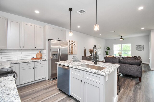 kitchen featuring pendant lighting, sink, stainless steel appliances, light stone countertops, and an island with sink