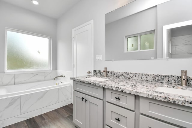 bathroom featuring a relaxing tiled tub, vanity, and wood-type flooring