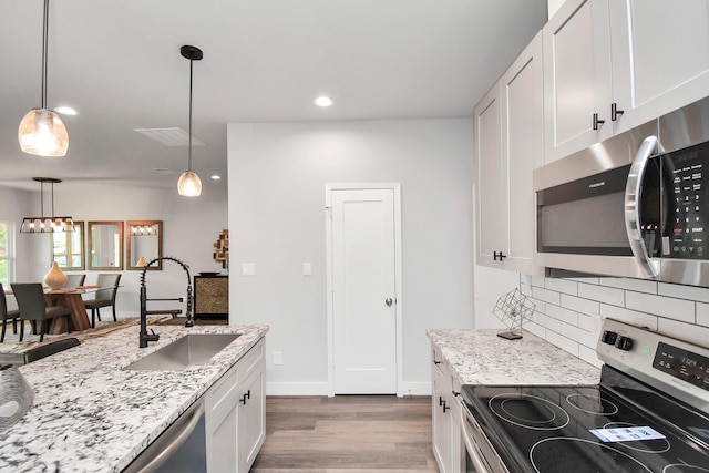 kitchen with appliances with stainless steel finishes, pendant lighting, white cabinetry, sink, and light stone counters